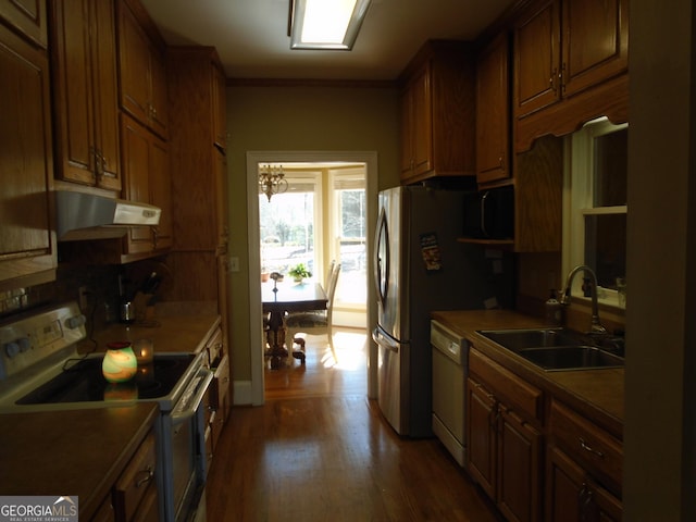 kitchen featuring a sink, under cabinet range hood, brown cabinets, white appliances, and dark wood-style flooring