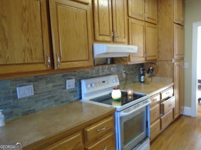 kitchen featuring decorative backsplash, light countertops, light wood-style floors, under cabinet range hood, and white electric range