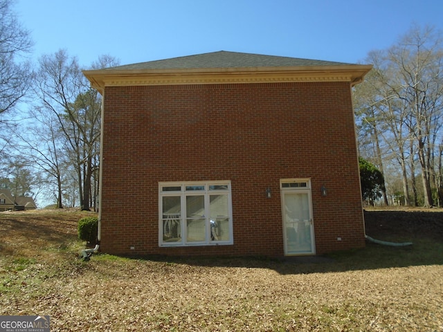 back of house with brick siding and a lawn