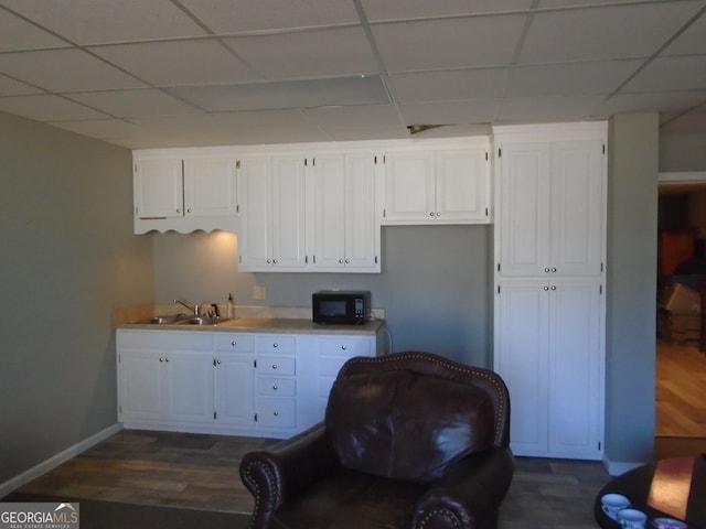 kitchen featuring black microwave, dark wood-style floors, white cabinets, a paneled ceiling, and a sink