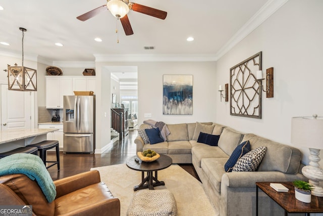 living room featuring ceiling fan with notable chandelier, dark wood-style floors, visible vents, and ornamental molding