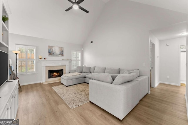 living area featuring a ceiling fan, baseboards, high vaulted ceiling, light wood-style flooring, and a fireplace with flush hearth