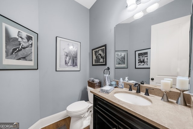 half bath with vanity, toilet, wood finished floors, and baseboards