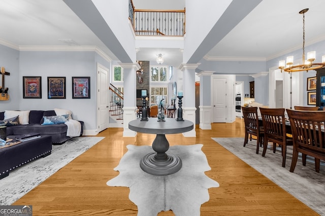 dining area featuring decorative columns, light wood finished floors, an inviting chandelier, and stairway