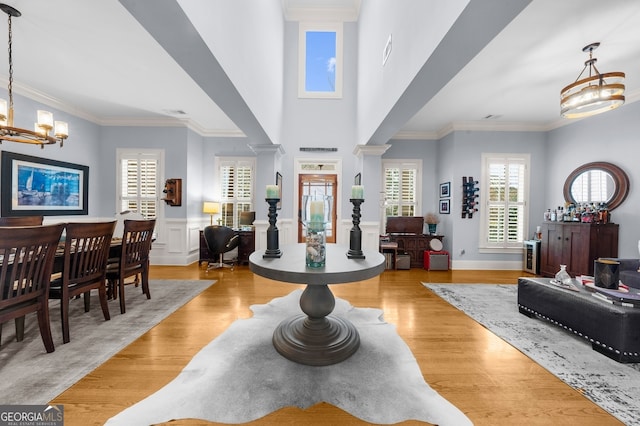 entryway featuring light wood finished floors, a wainscoted wall, ornamental molding, an inviting chandelier, and ornate columns