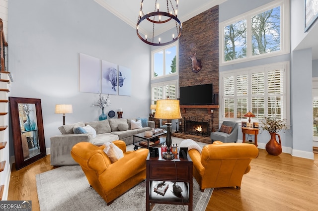 living area with a notable chandelier, wood finished floors, stairway, a fireplace, and crown molding