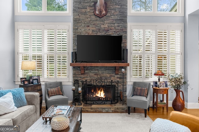 living area with a stone fireplace, baseboards, and wood finished floors