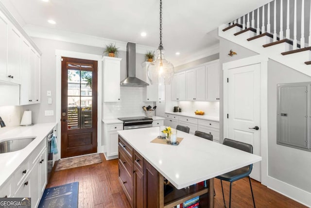 kitchen featuring wall chimney range hood, electric panel, a sink, appliances with stainless steel finishes, and a kitchen breakfast bar