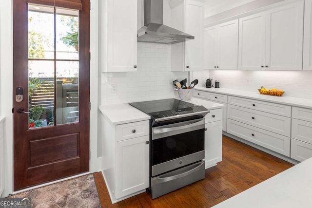 kitchen featuring wall chimney range hood, stainless steel electric stove, dark wood finished floors, white cabinets, and light countertops