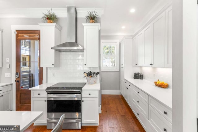 kitchen featuring wall chimney range hood, dark wood-style floors, stainless steel range with electric cooktop, white cabinets, and light countertops