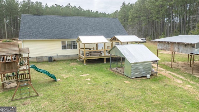 back of house with roof with shingles, a yard, an outdoor structure, a storage shed, and a playground