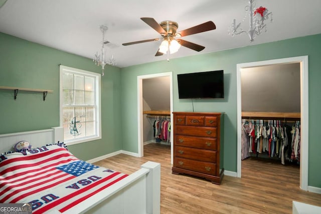 bedroom with wood finished floors, visible vents, baseboards, a closet, and a walk in closet