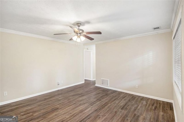 empty room with dark wood finished floors, visible vents, crown molding, and baseboards