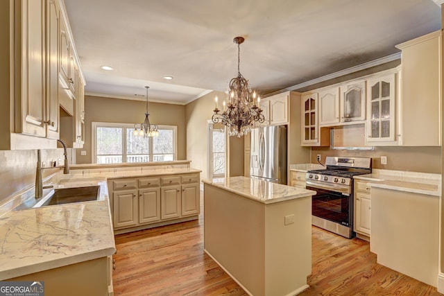 kitchen featuring a kitchen island, light wood-style flooring, appliances with stainless steel finishes, a notable chandelier, and a sink