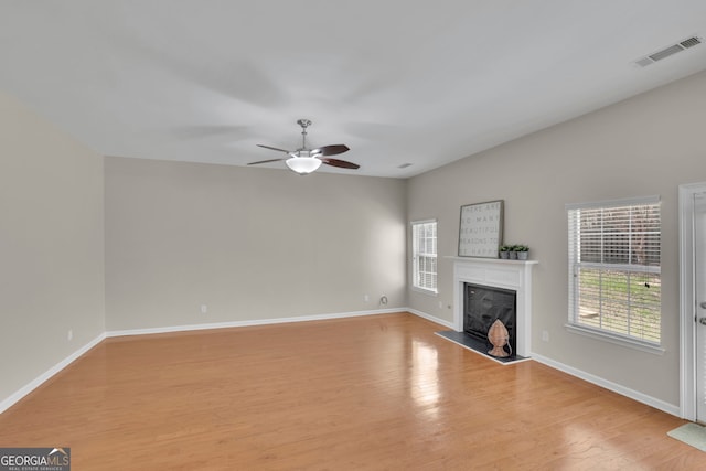 unfurnished living room with visible vents, light wood-style flooring, a fireplace, baseboards, and ceiling fan