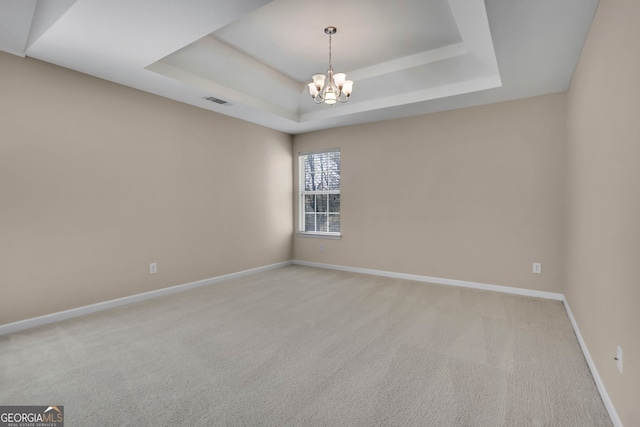 spare room with visible vents, a tray ceiling, an inviting chandelier, carpet flooring, and baseboards