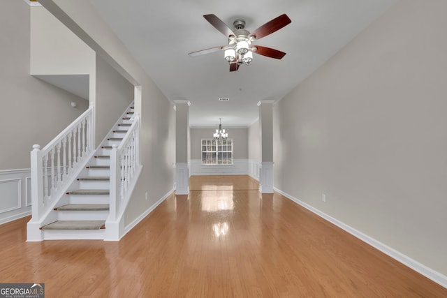 entryway featuring light wood-type flooring, a wainscoted wall, ceiling fan with notable chandelier, stairway, and a decorative wall