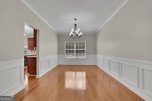 unfurnished dining area with a wainscoted wall, a notable chandelier, light wood-style flooring, and crown molding