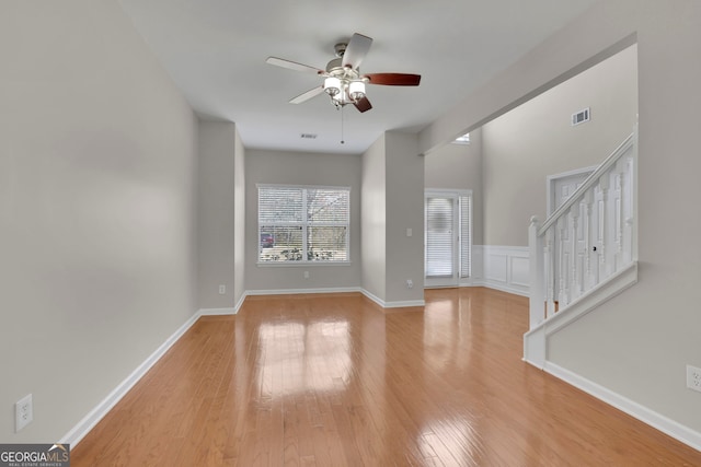 unfurnished living room with light wood-type flooring, visible vents, baseboards, ceiling fan, and stairs