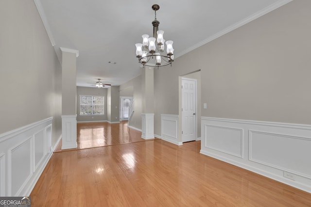 unfurnished dining area with light wood finished floors, ceiling fan with notable chandelier, ornate columns, and ornamental molding