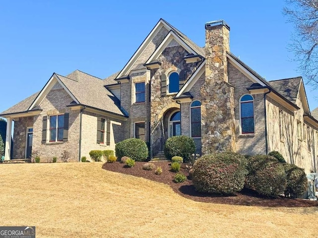 view of front of house with stone siding, brick siding, a chimney, and a front yard