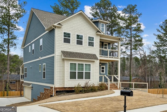 view of front facade with driveway, a shingled roof, a balcony, and fence