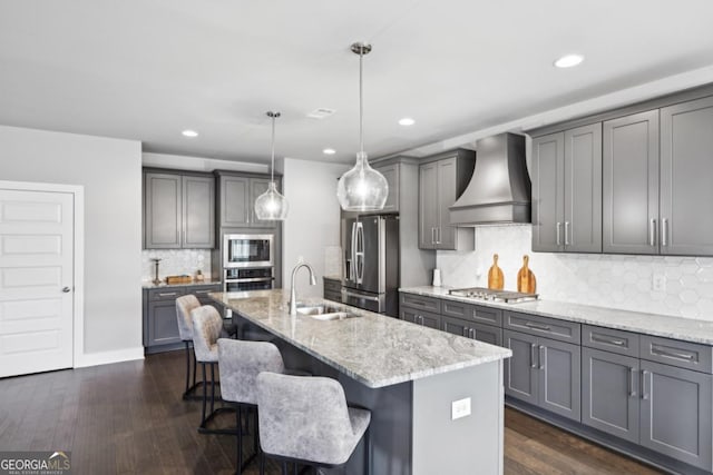 kitchen with a breakfast bar area, light stone counters, appliances with stainless steel finishes, custom exhaust hood, and a sink