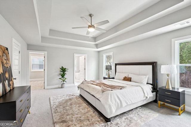 carpeted bedroom with ensuite bath, multiple windows, baseboards, and a tray ceiling