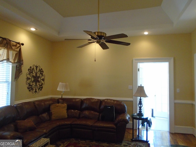 living area with a ceiling fan, a tray ceiling, recessed lighting, and wood finished floors