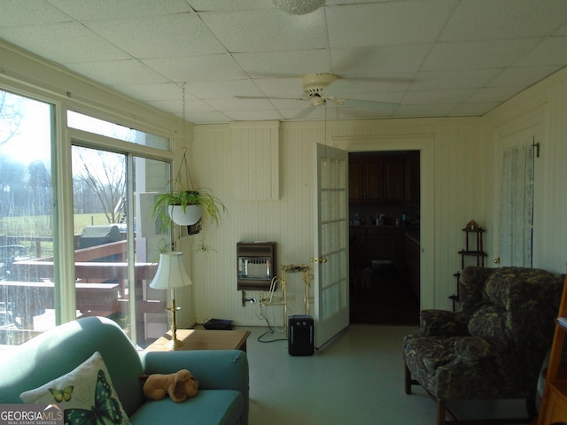 living area with heating unit, a paneled ceiling, concrete floors, and ceiling fan