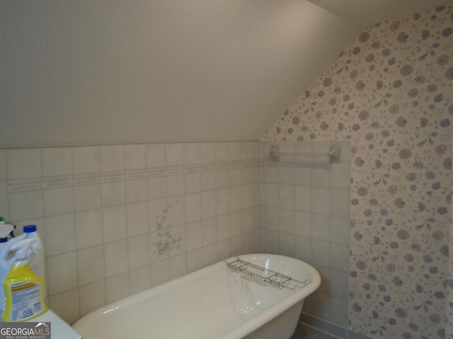 bathroom featuring a freestanding tub, a textured ceiling, tile walls, and vaulted ceiling