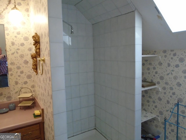 bathroom featuring vaulted ceiling, a tile shower, and wallpapered walls