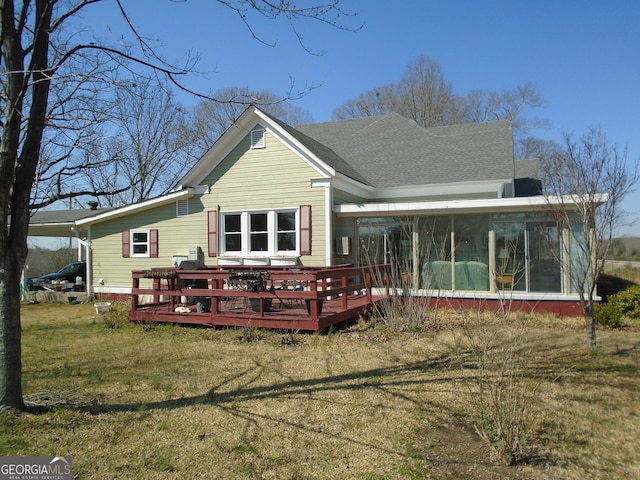 back of property featuring a deck, a lawn, a sunroom, and a shingled roof