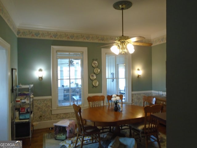 dining room with ornamental molding, ceiling fan, wainscoting, and wallpapered walls