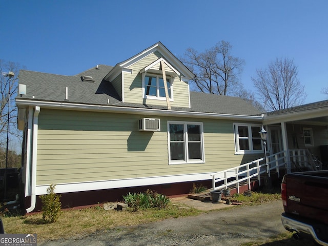 view of property exterior with a shingled roof and a wall unit AC