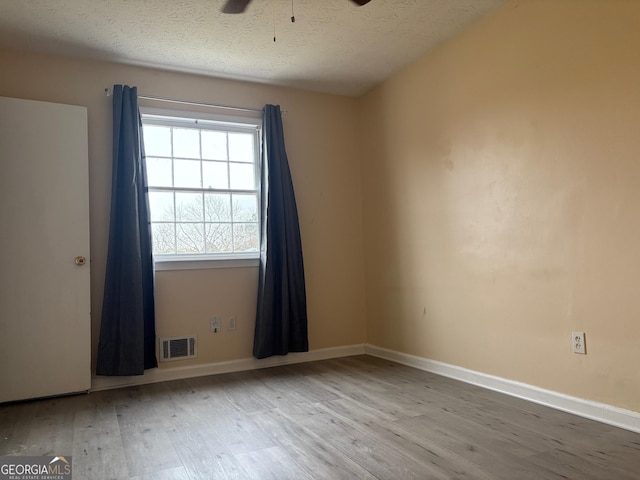 empty room with visible vents, a textured ceiling, a ceiling fan, and wood finished floors