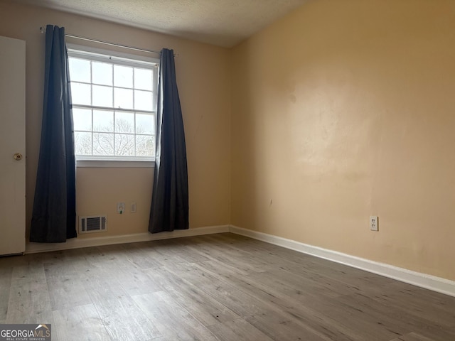 unfurnished room with a textured ceiling, wood finished floors, visible vents, and baseboards