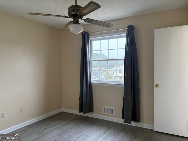 unfurnished room featuring wood finished floors, a ceiling fan, visible vents, and baseboards