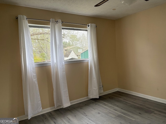 spare room with baseboards, a textured ceiling, wood finished floors, and a ceiling fan