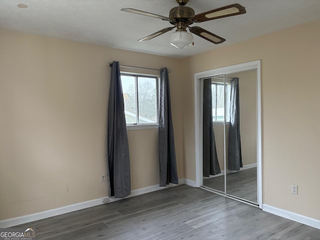 unfurnished bedroom with wood finished floors, baseboards, ceiling fan, a closet, and a textured ceiling