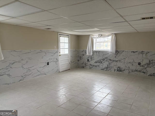 below grade area with a wainscoted wall, a paneled ceiling, and visible vents