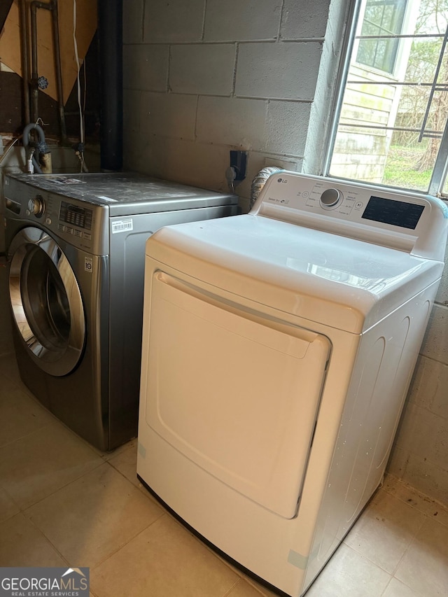 clothes washing area featuring laundry area, concrete block wall, separate washer and dryer, and light tile patterned flooring