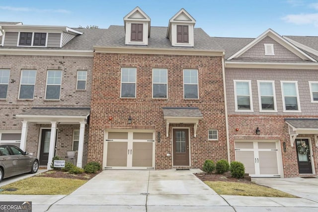 townhome / multi-family property with brick siding, a garage, driveway, and roof with shingles