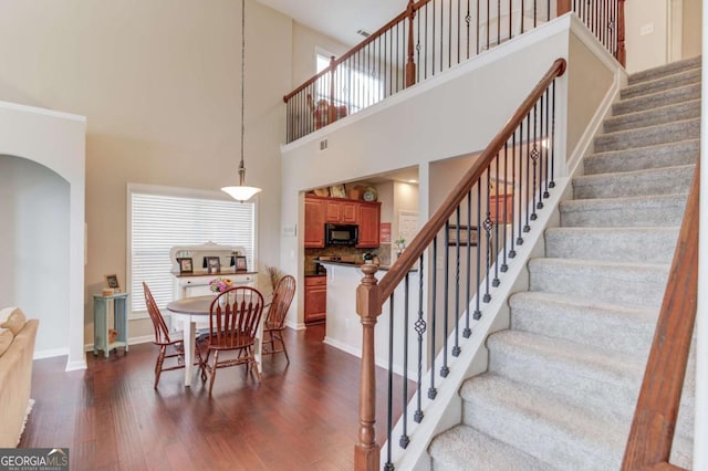 staircase featuring arched walkways, visible vents, baseboards, and wood finished floors