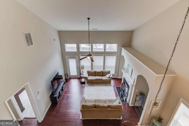 living room featuring visible vents, a fireplace, ceiling fan, dark wood-type flooring, and a towering ceiling