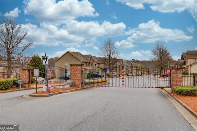 view of road with a gated entry, a residential view, curbs, traffic signs, and a gate