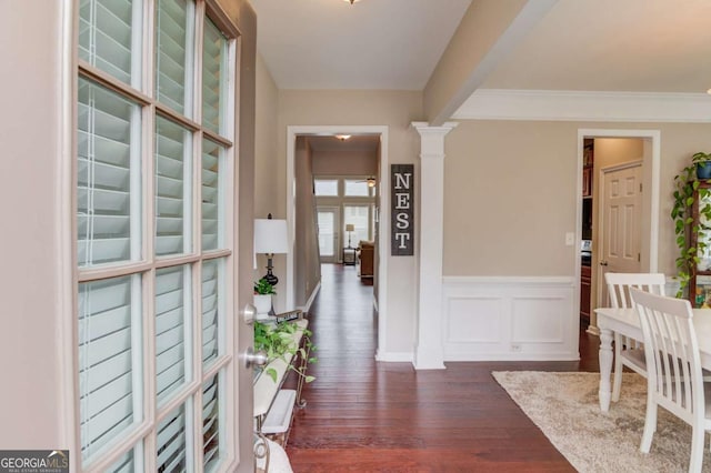 entryway with dark wood-type flooring, a decorative wall, crown molding, wainscoting, and decorative columns