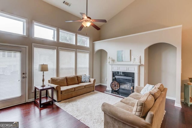 living room featuring visible vents, a fireplace with flush hearth, arched walkways, and dark wood-style floors