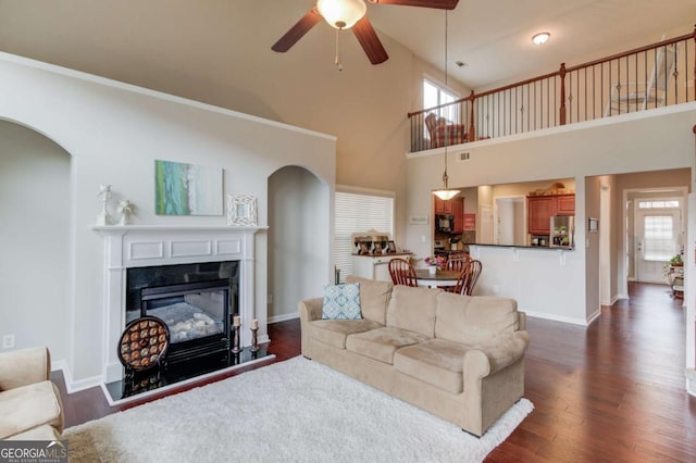 living room with baseboards, dark wood finished floors, arched walkways, a glass covered fireplace, and a ceiling fan