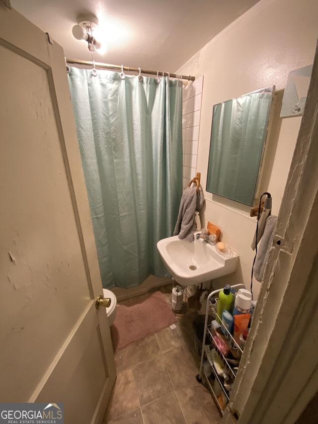 bathroom featuring curtained shower, toilet, tile patterned flooring, and a sink